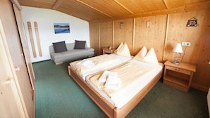 A wooden room with a bed, a sofa, a nightstand, and a wall-mounted picture.