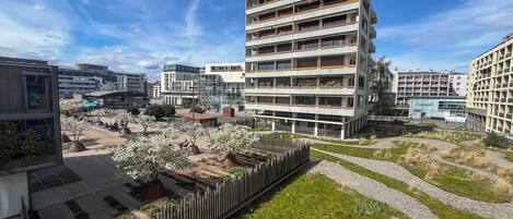 A multi-story residential building with balconies, surrounded by a landscaped area with trees and a pathway.
