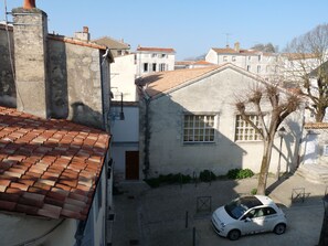 Una calle estrecha con arquitectura europea tradicional, un coche blanco estacionado al lado y un cielo despejado.
