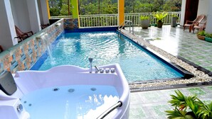 A hot tub with a waterfall feature, a pool, and a patio area with chairs and potted plants. - Grand Adams Peak Hotel (Nallathanniya)