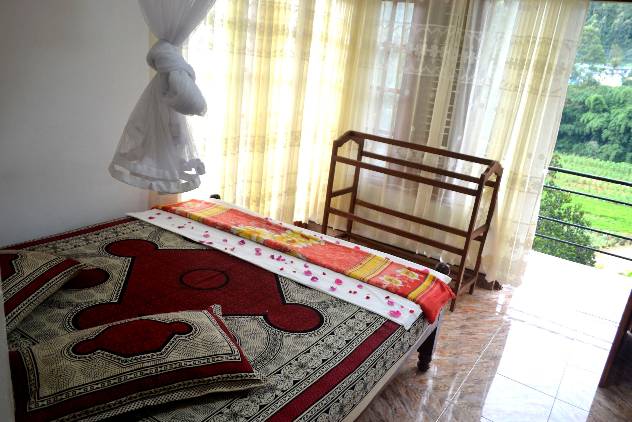 A bed with a red and white patterned bedspread, a wooden headboard, and a balcony with a view of greenery.