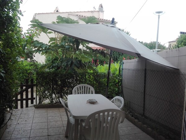 Un patio al aire libre con mesa y sillas, una zona cubierta y una cerca de malla metálica.