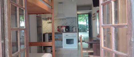 A compact kitchen with a built-in oven, a dining table with chairs, and a bunk bed with a mattress.