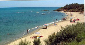 Una playa con gente tomando el sol, nadando y barcos en el agua.
