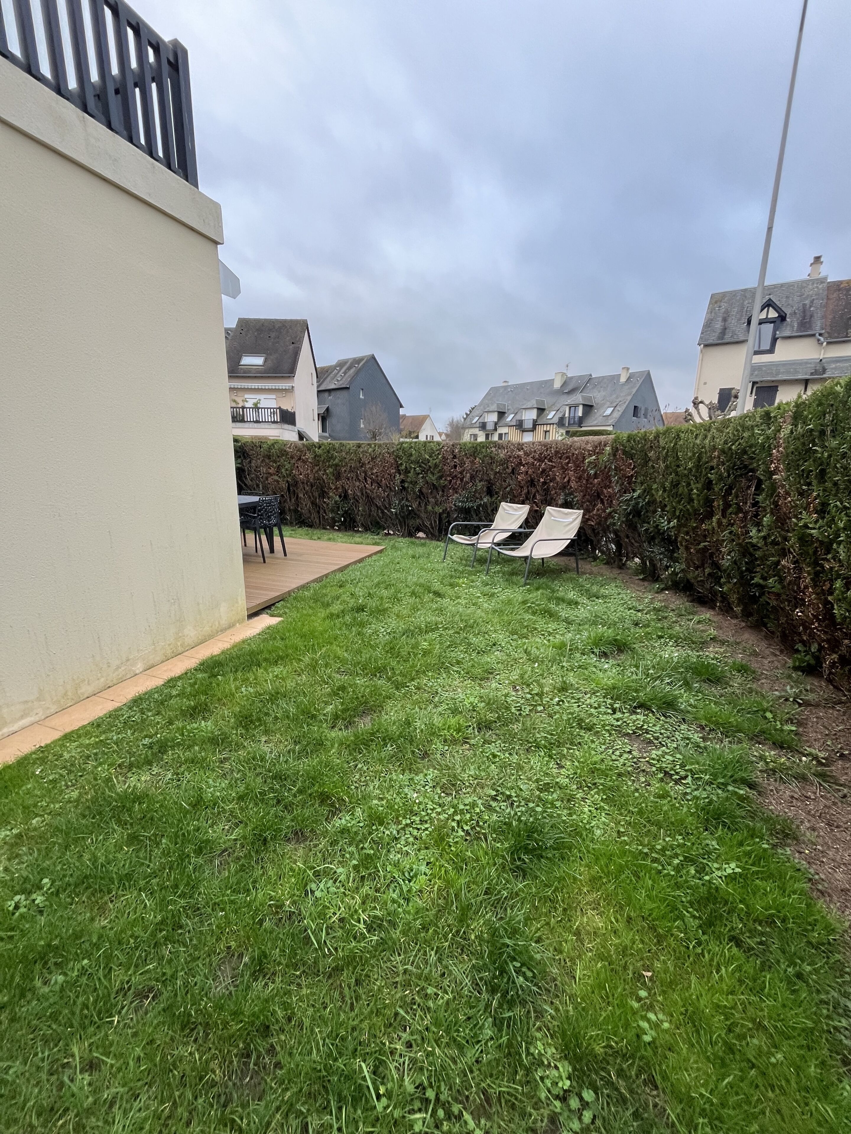 A residential backyard with a grassy lawn, a wooden deck, and a hedge.