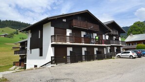 Een gebouw met twee verdiepingen, voorzien van een balkon op de bovenste etage, een garage en een parkeerplaats met auto's.