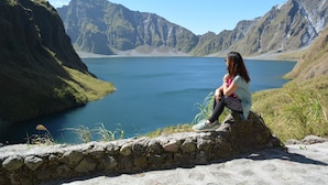 Una persona seduta su una sporgenza di pietra con vista su un lago e montagne sullo sfondo.
