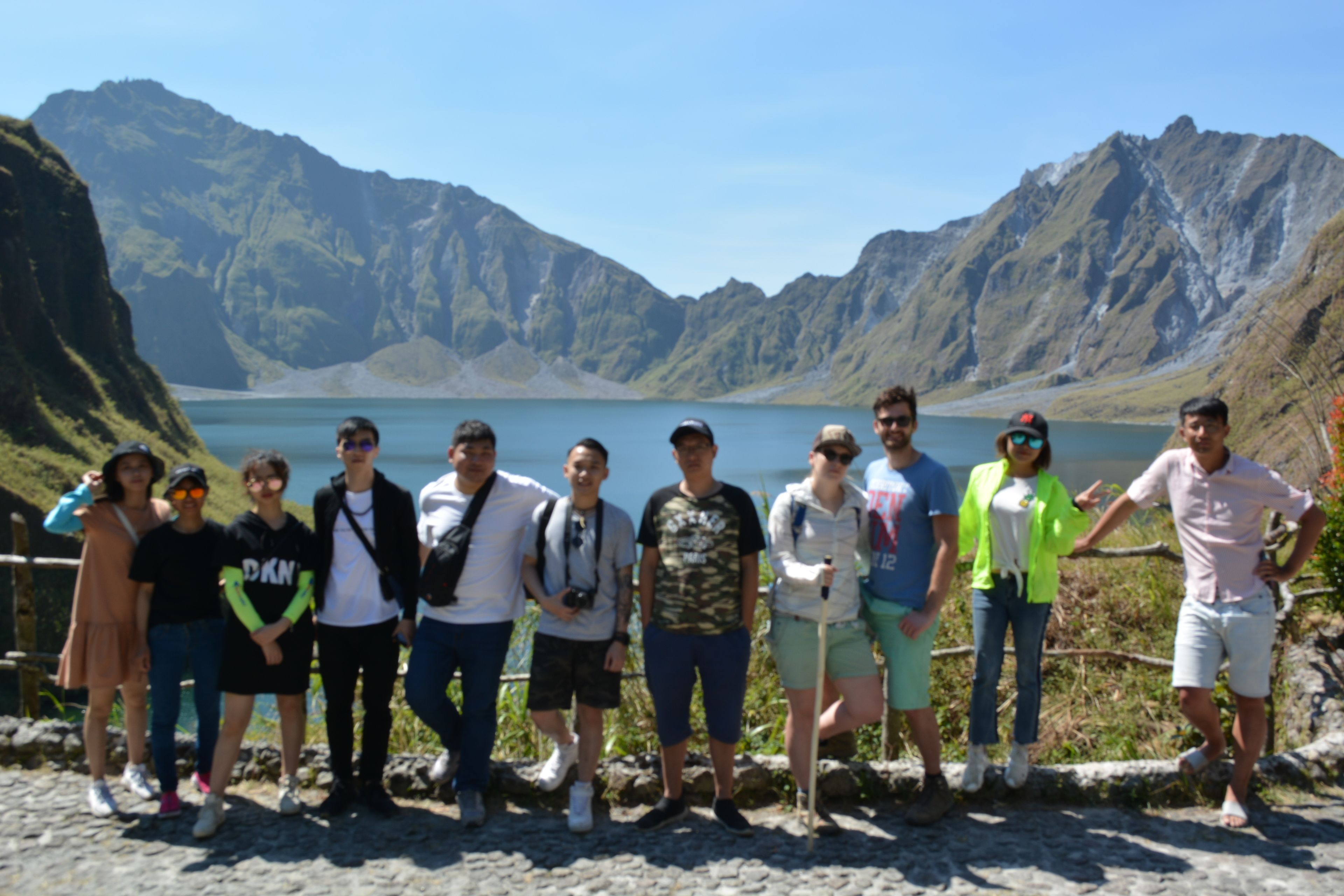 A group of people standing on a rocky ledge with a mountainous backdrop and a body of water.