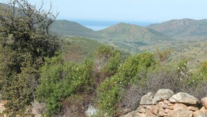 Paisaje montañoso con un muro de piedra en primer plano y vistas a colinas ondulantes y una masa de agua distante.