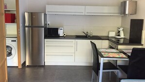 Una cocina compacta con refrigerador, microondas, cafetera y un comedor con mesa y sillas.
