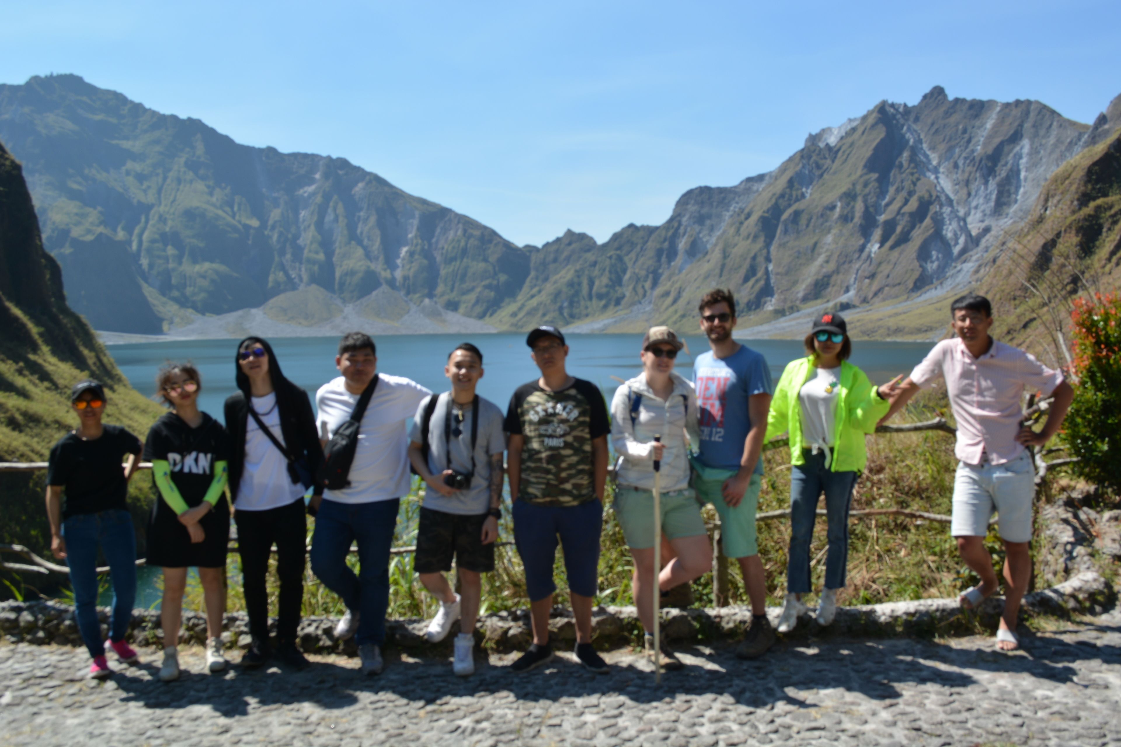 Un grupo de personas sobre un sendero rocoso, con montañas al fondo y una masa de agua.