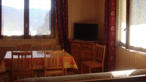 Una stanza con rivestimenti in legno, un tavolo da pranzo, sedie, una televisione e ampie finestre con tende.
