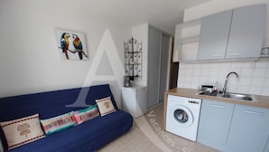 A compact living space with a blue sofa, a washing machine, and a kitchenette.