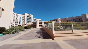 A modern building with multiple floors, a paved walkway, and a fenced garden area.