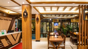 Zona de recepción de hotel con un mostrador de madera, una alfombra roja y un área de estar con mesas y sillas de madera.