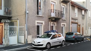 Un coche blanco estacionado en una calle con un edificio que tiene balcones y una entrada protegida por una reja.