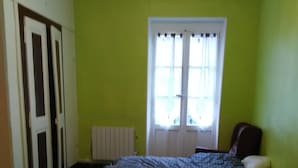Una habitación con dos camas, un radiador, una ventana con cortinas y una puerta.