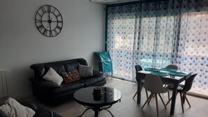 Una sala de estar con un sofá de cuero negro, una mesa redonda de centro, una mesa de comedor con sillas y un ventanal con cortinas estampadas.