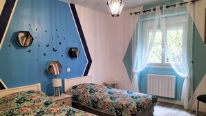 Una habitación con dos camas, una pared azul decorada con mariposas, una ventana con cortinas translúcidas y una lámpara colgante.