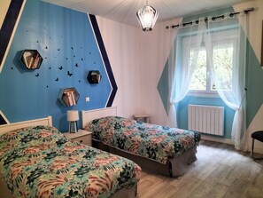 A room with two beds, a blue wall with butterfly decals, a window with sheer curtains, and a hanging light fixture.