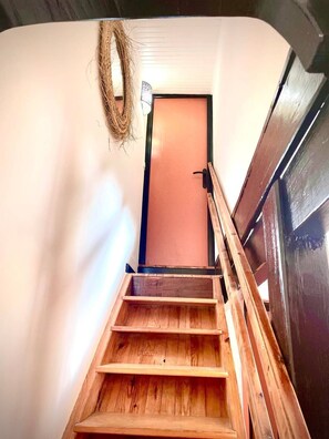 A wooden staircase leading to a door with a rope hanging on the wall.