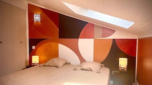 Un dormitorio con cama, dos lámparas de noche, un tragaluz y una pared con patrones geométricos abstractos.