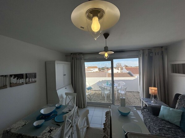 Una habitación con una mesa de comedor, sillas, un sofá, una lámpara y vistas a través de un ventanal.