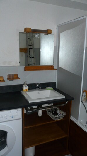 Une petite salle de bain avec un lavabo blanc, un miroir au-dessus et une étagère en bois.