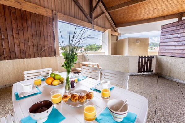 A breakfast table set with croissants, fruit, and juice, with a view of the outdoors.