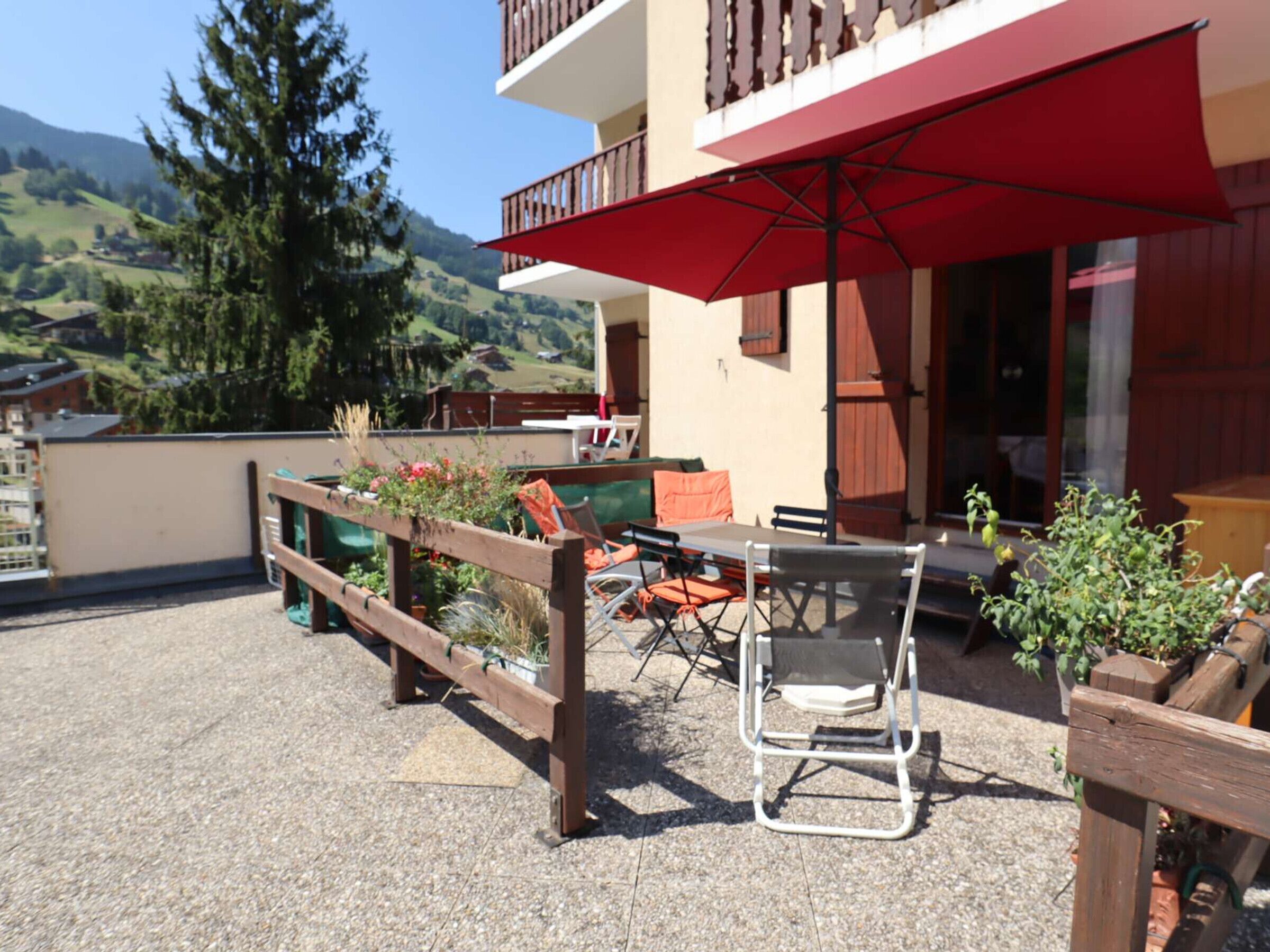 Une terrasse aménagée avec du mobilier d’extérieur, un parasol rouge et une vue sur le paysage environnant.