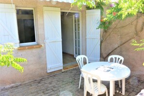Une terrasse avec une table ronde et quatre chaises, une porte et une fenêtre.