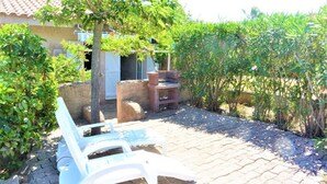 Eine Terrasse mit zwei weißen Liegestühlen, einer Steinsitzbank und einem kleinen Tisch.