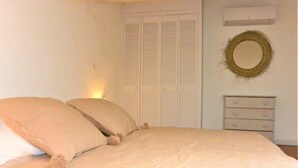 Ein Schlafzimmer mit einem Bett, zwei Kissen, einem Schminktisch, einem Spiegel und einem Schrank mit Klappläden.