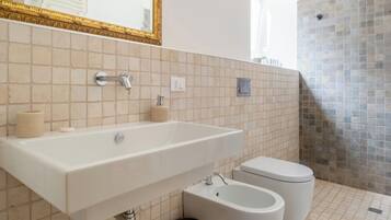 Un baño moderno con un espejo grande, un lavamanos, dos bidés, un cesto de basura y una zona de ducha.