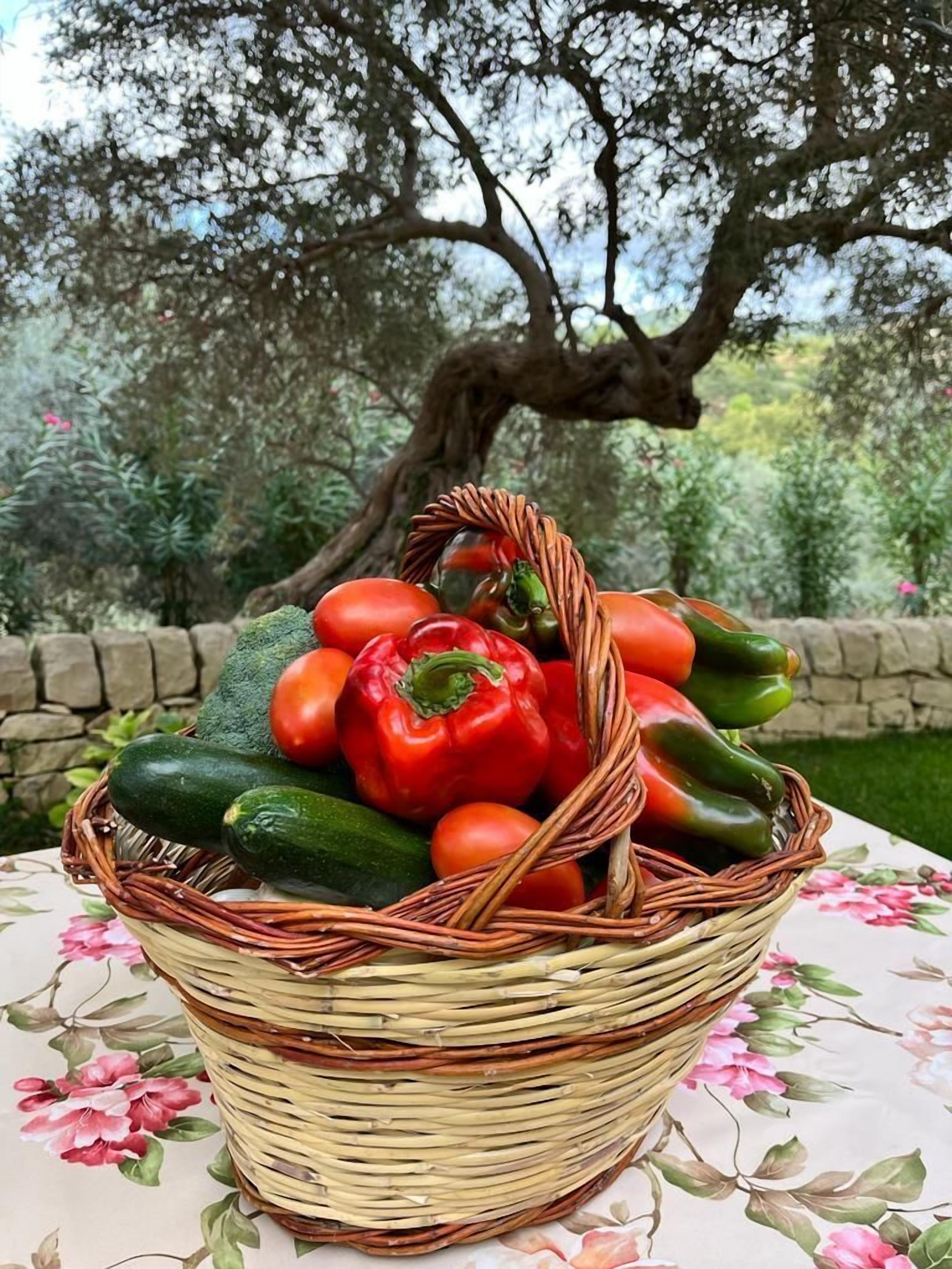 Una cesta de mimbre llena de verduras sobre una mesa con mantel floreado.