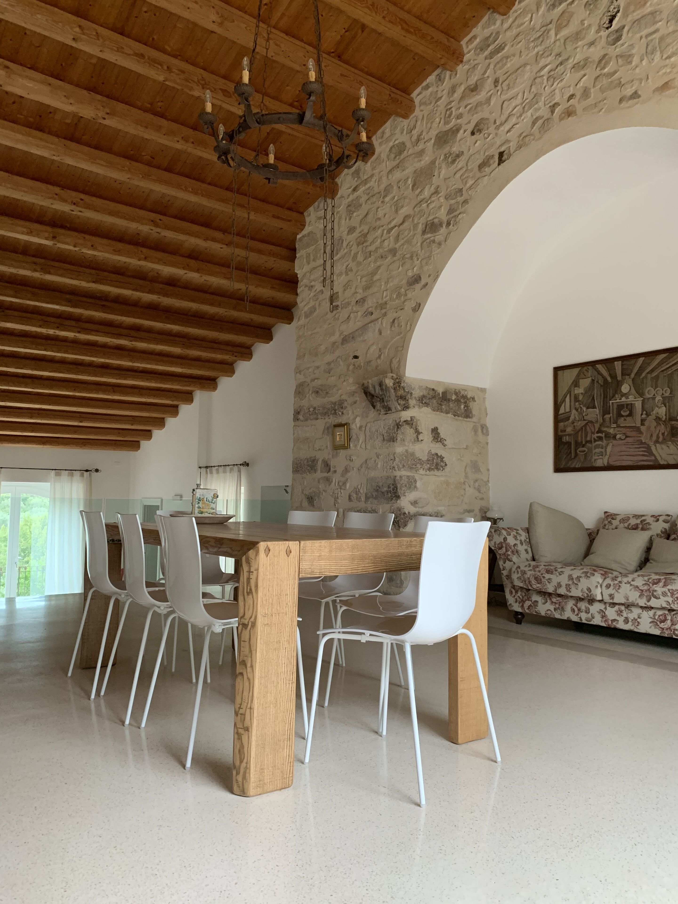 A dining area with a wooden table and chairs, a chandelier, and a stone wall.