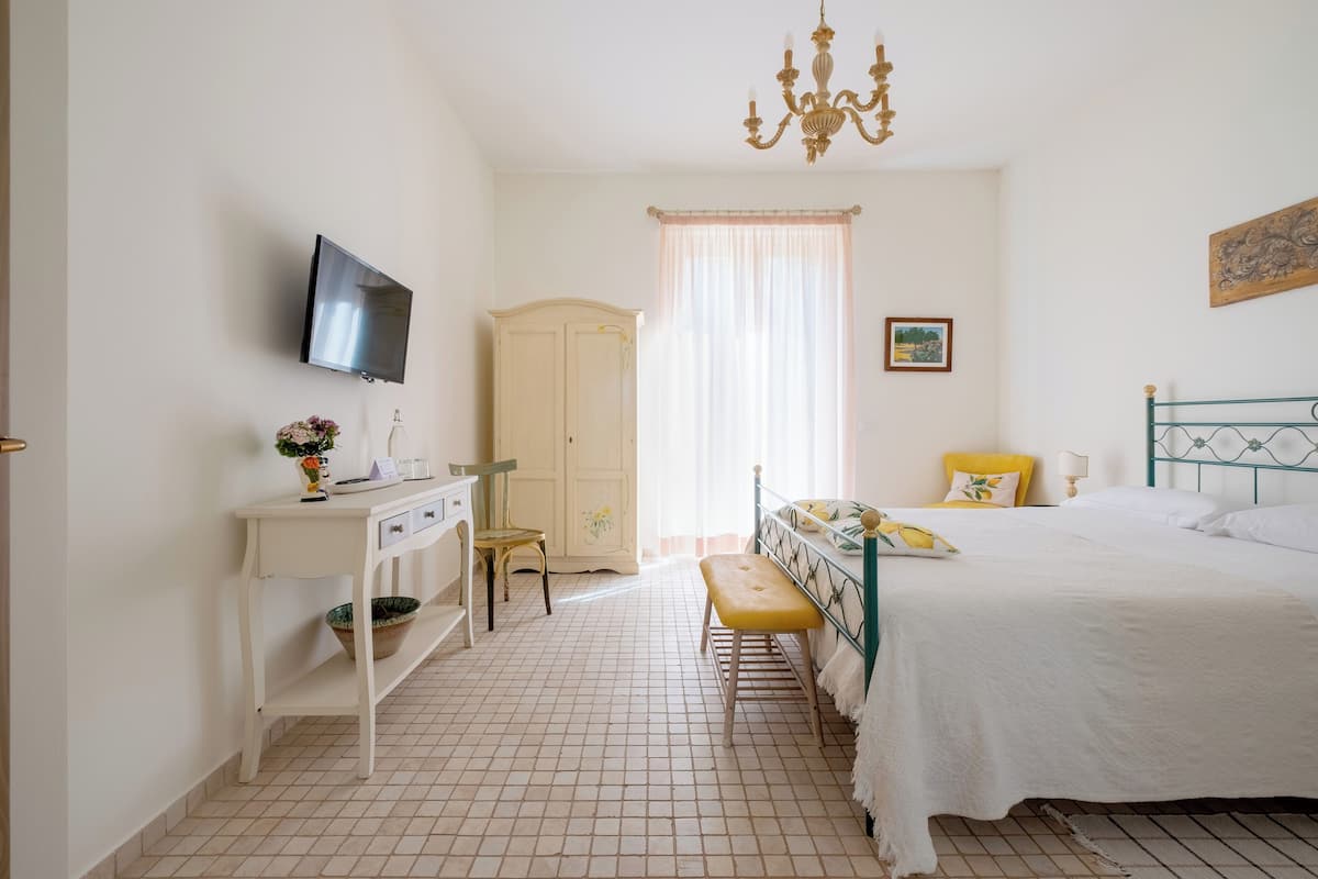 A bedroom with a bed, a desk, a television, and a window with curtains.