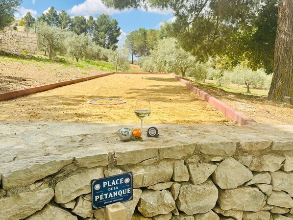 Un terrain de pétanque avec un mur de pierre au premier plan et un panneau indiquant l’emplacement.
