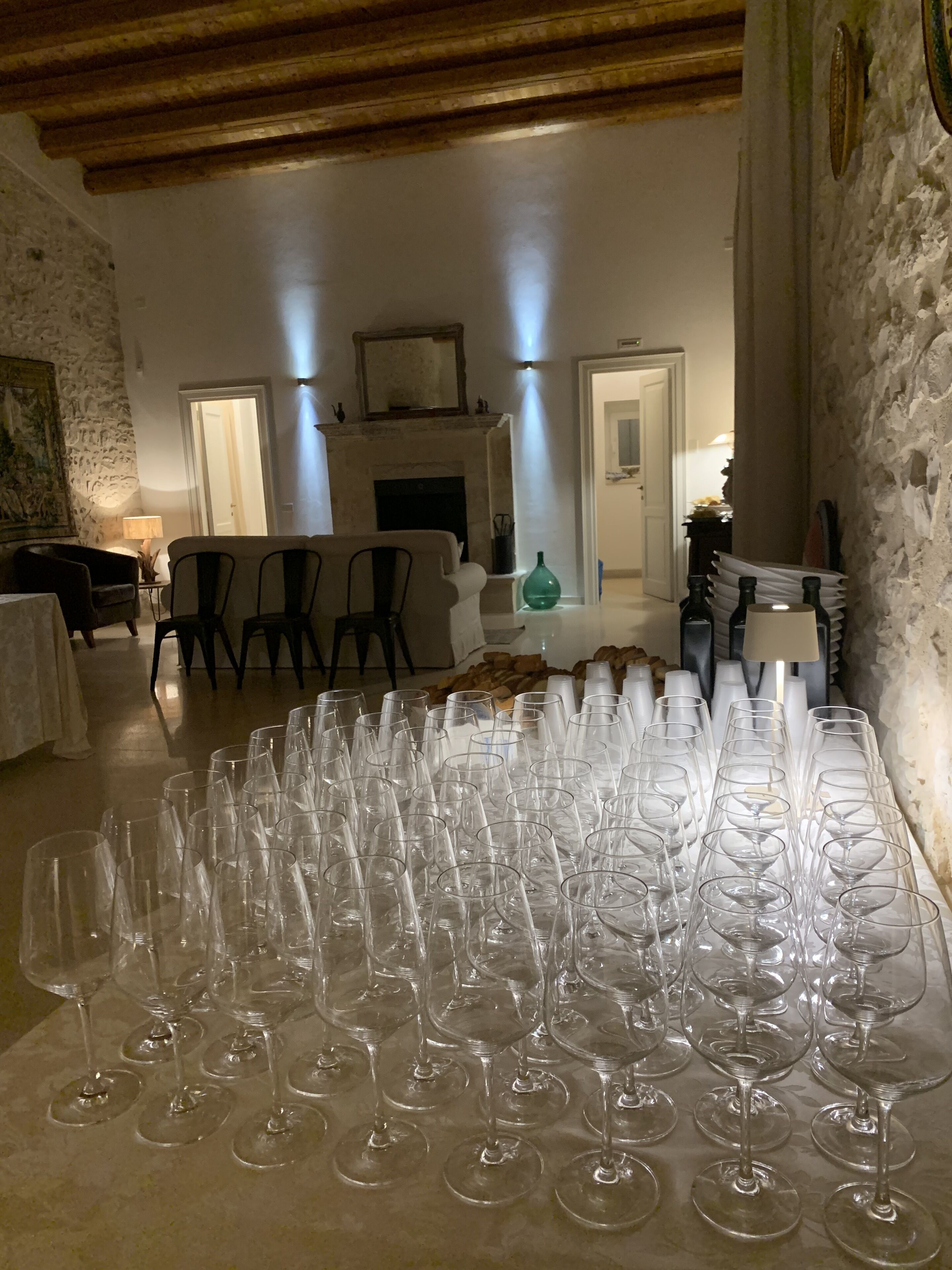 A room with a large table of empty wine glasses, a fireplace, and stone walls.