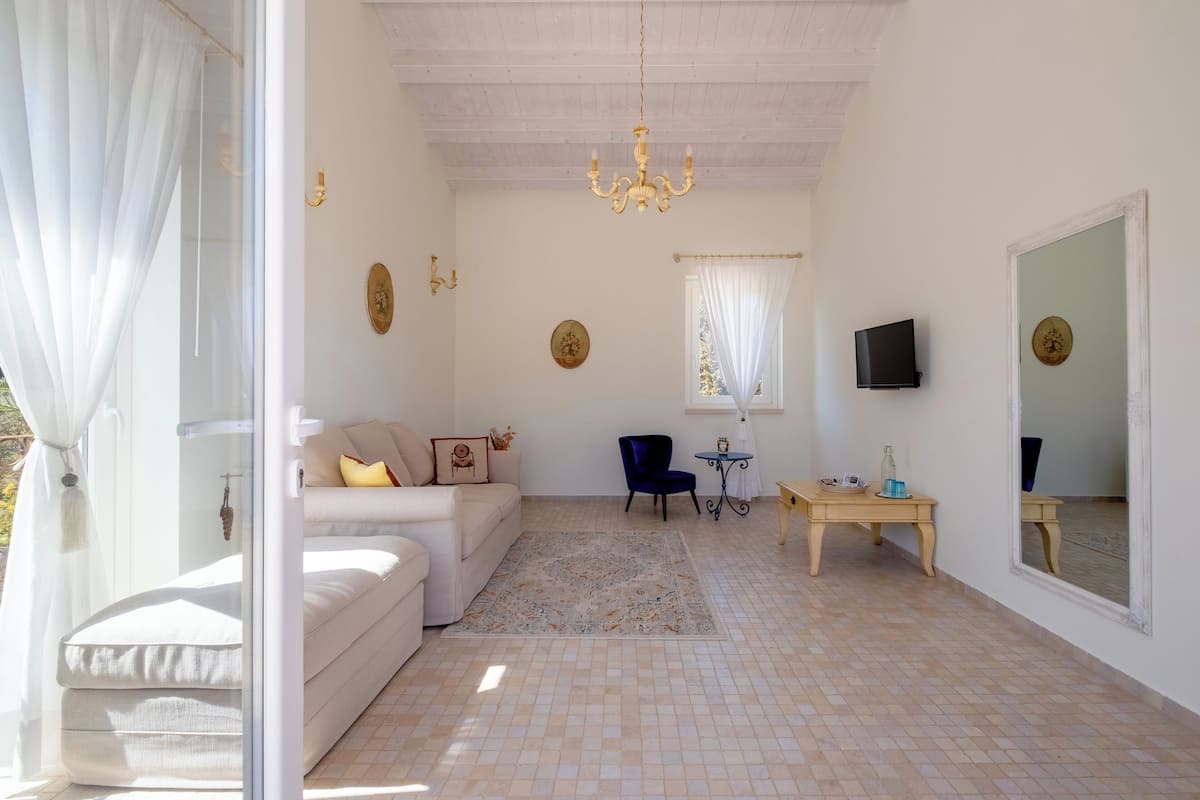 A living room with a sofa, a chair, a small table, a TV, and a mirror.