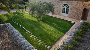 Un bâtiment en pierre avec un toit en tuiles, une pelouse bien entretenue et un mur de pierre qui entoure la propriété.