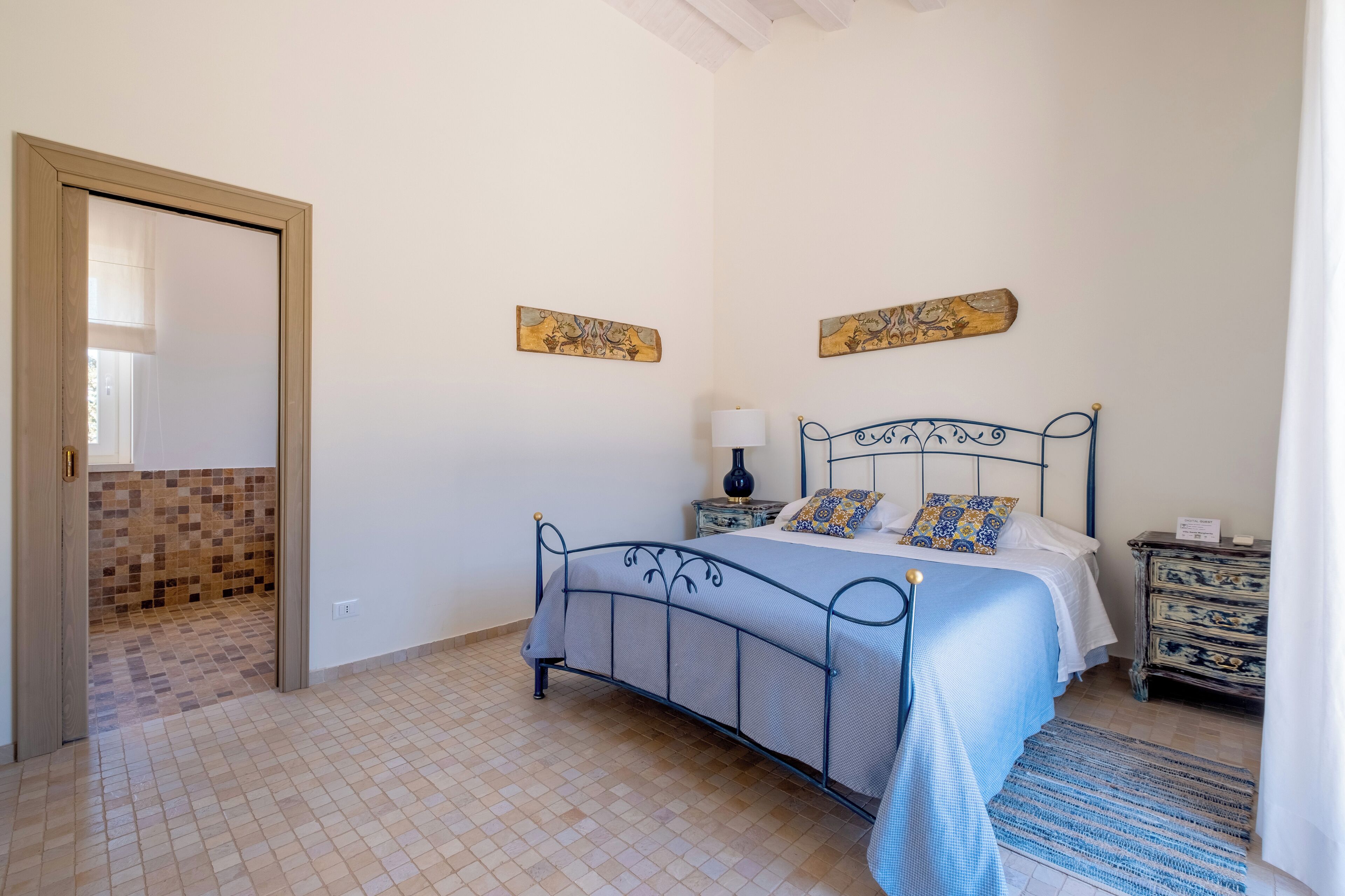 A bedroom with a bed, bedside table, lamp, and decorative wall pieces.