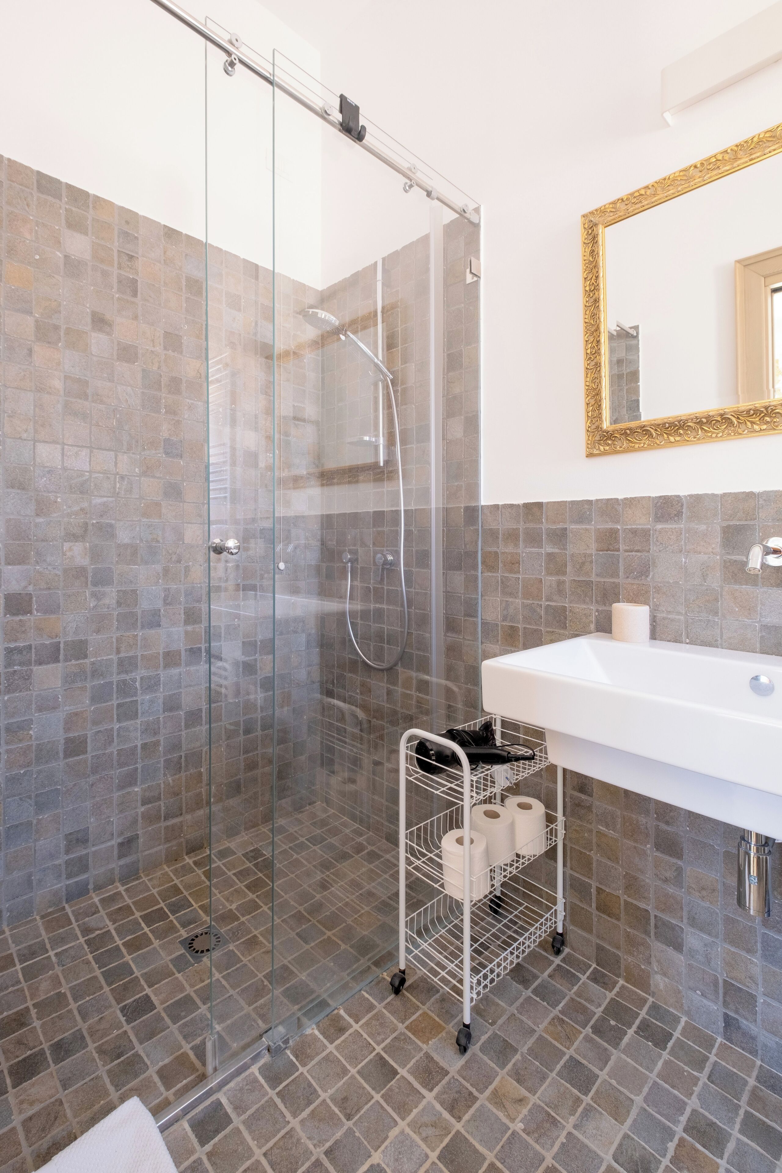 A modern bathroom with a glass-enclosed shower, a white sink, and a tiled floor.