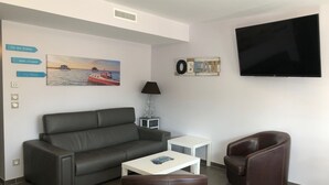 A modern living room with a grey sofa, a white coffee table, a brown leather armchair, and a TV mounted on the wall.