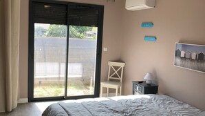 A bedroom with a large bed, a chair, a nightstand, a ceiling light fixture, and a view through a sliding door.