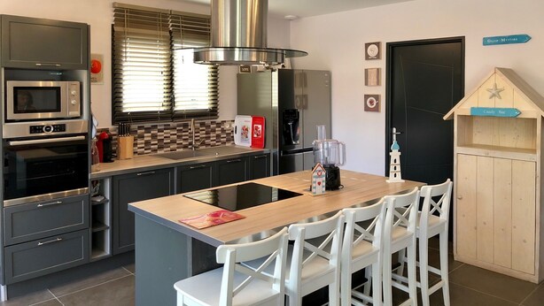 A modern kitchen with a central island, stainless steel appliances, and a wooden bar area.