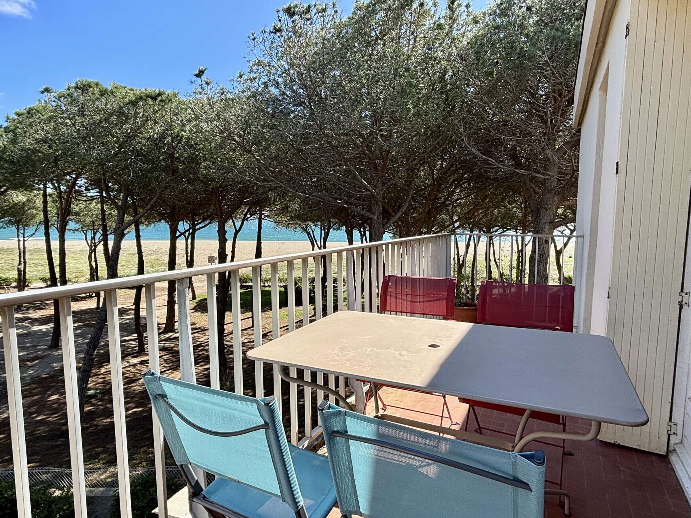 A balcony with a table and chairs, overlooking a beach and trees.