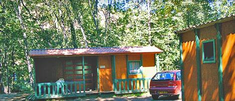 A small cabin with a porch and a car parked in front.