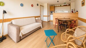Un salon comprenant un canapé, une petite table, des chaises en osier, un coin cuisine avec des meubles en bois et un four à micro-ondes.