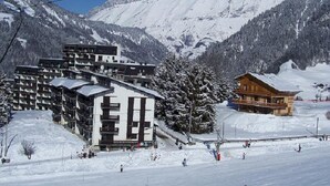A ski resort with modern buildings, a ski lift, and snow-covered mountains in the background.